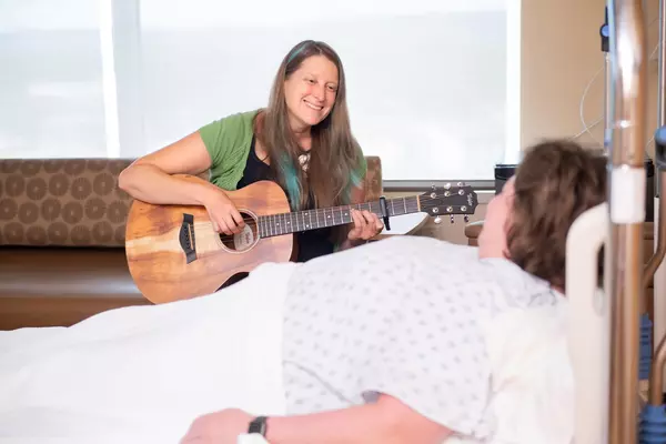 Certified music practitioner playing guitar for patient in patient room.