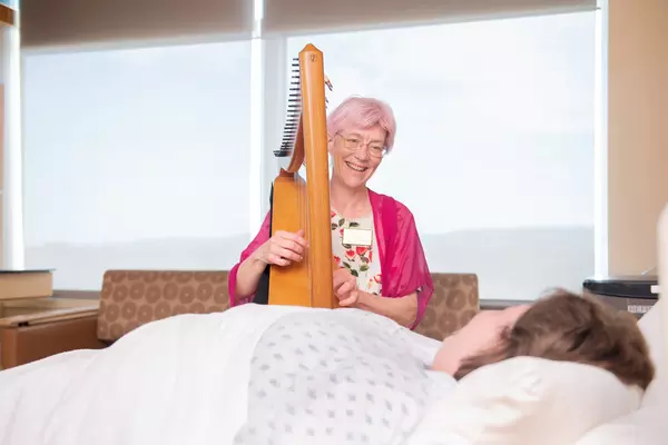Certified music practitioner playing harp to patient in patient room.