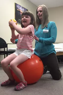 Physical therapist assisting child on exercise ball.