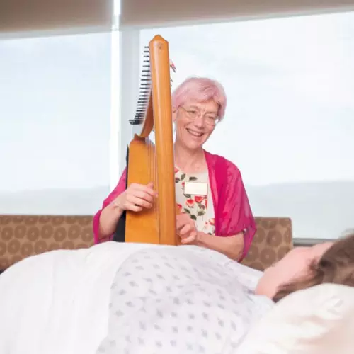Music therapist playing harp to patient in the hospital.