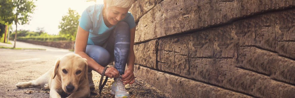 woman kneeling down tying her shoes while her dog sits nearby