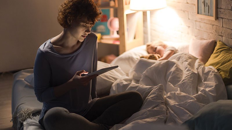 mother sitting on daughter's bed looking at tablet
