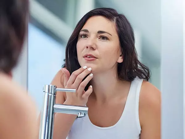 woman looking in the mirror at acne scars