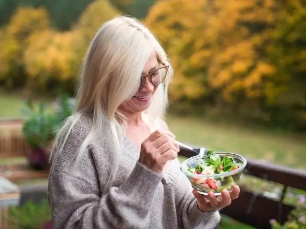 woman standing on balcony eating a salad