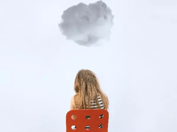 Adolescent girl sitting on a chair with a cloud hovering over her.
