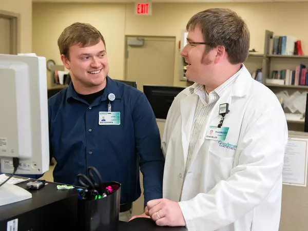 Pharmacist working with resident at computer and smiling.