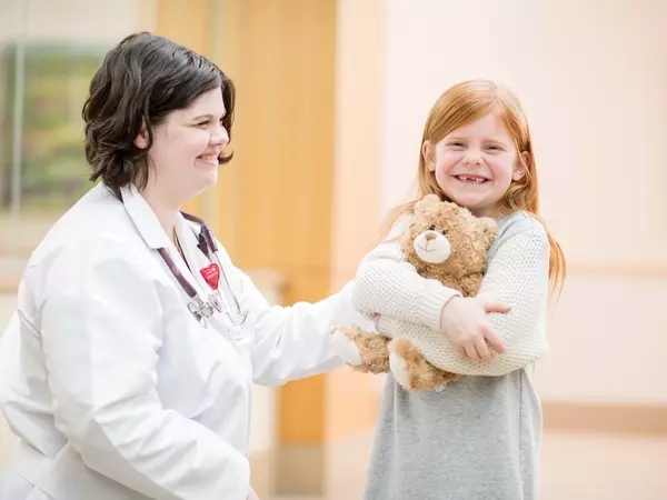 Doctor smiling at young child hugging her teddy bear.