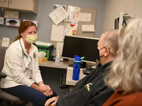 Nurse wearing mask meeting with patients in exam room.