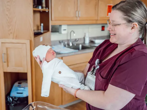 Nurse holding newborn in hospital room.