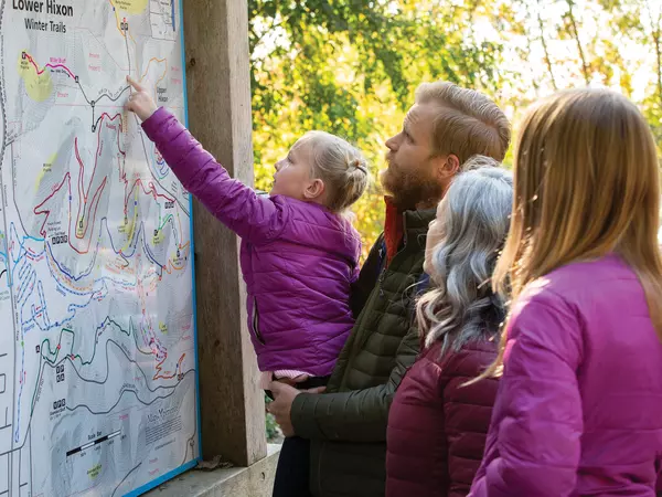 Family of four looking at hiking trails map in autumn.