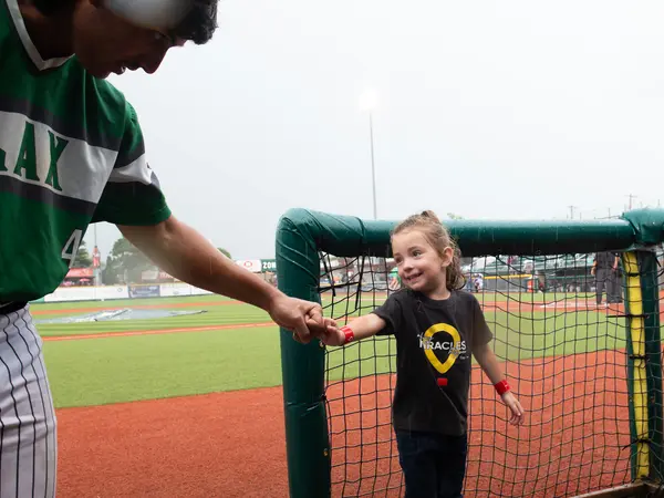 Smiling young girl sharing knuckles with baseball player.