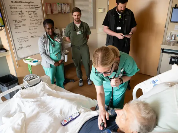 Internal Medicine resident listening to patient's heart in a hospital bed.