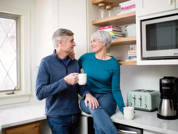 Senior couple smiling and looking at each other while holding coffee in the kitchen.
