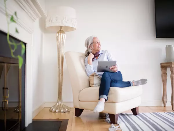 Happy senior woman holding a laptop seated in a white chair.