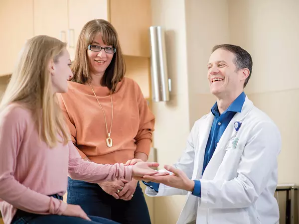 Male doctor giving exam to teenage girl patient while mother looks on.