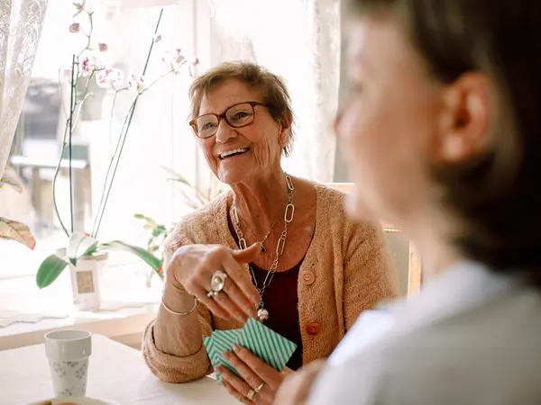 Smiling retired senior woman looking away while playing cards with social worker at nursing home.