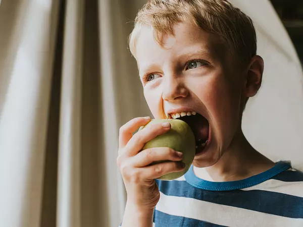 Fun image of a cute boy taking a huge bite of a green apple.