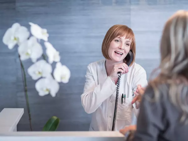 Receptionist greeting patient while on the phone.
