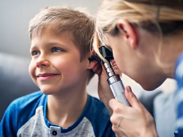 Doctor using otoscope to examine the young, smiling boy's ear.