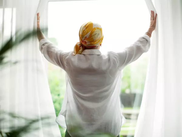 Rear view of mature woman opening curtains at window