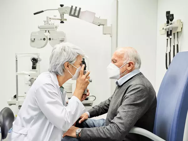 Doctor examining aged man through eye equipment