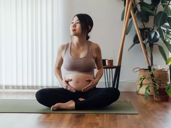 Beautiful young Asian pregnant woman resting after doing pregnancy yoga at home.