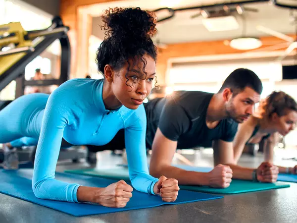 Slim women african american and caucasian ethnicity and muscular man in sportswear doing plank exercise on rubber mat in gym club.