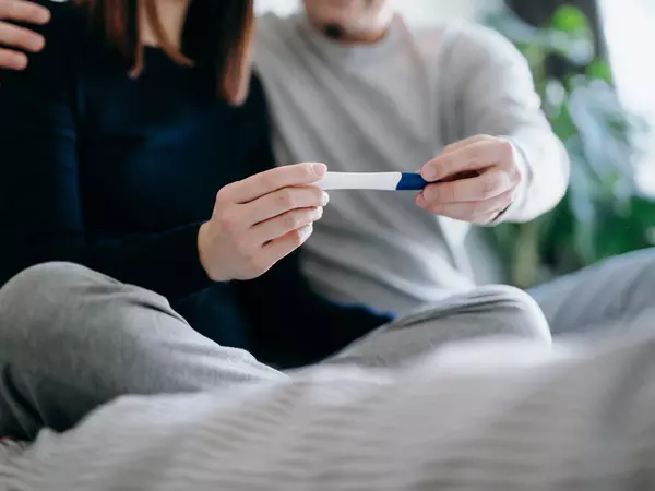 Couple sitting on the bed holding a pregnancy test together
