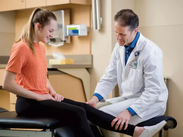Adult male doctor examining teenage girls knee.