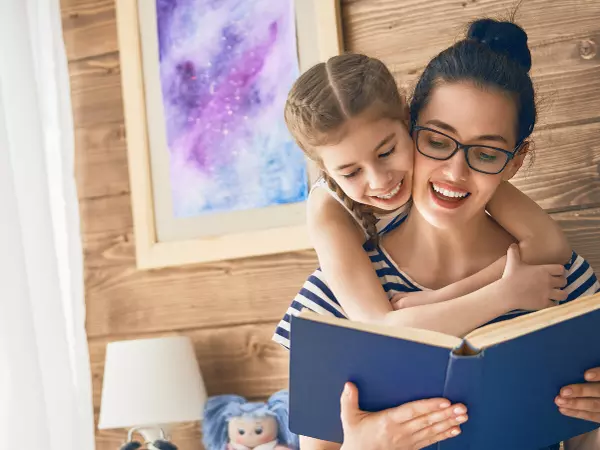 daughter leans over mother reading a book