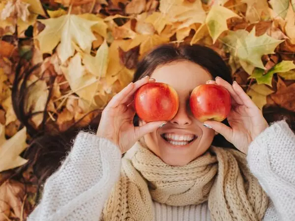 women laying in fall leaves putting apples to her eyes