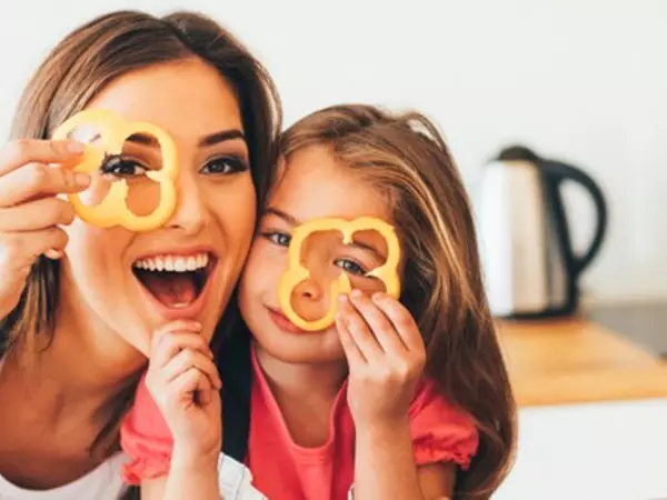 smiling mom and daughter holding a slice of pepper over an eye