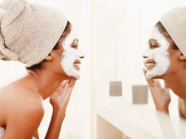 smiling woman applying face mask while looking in mirror