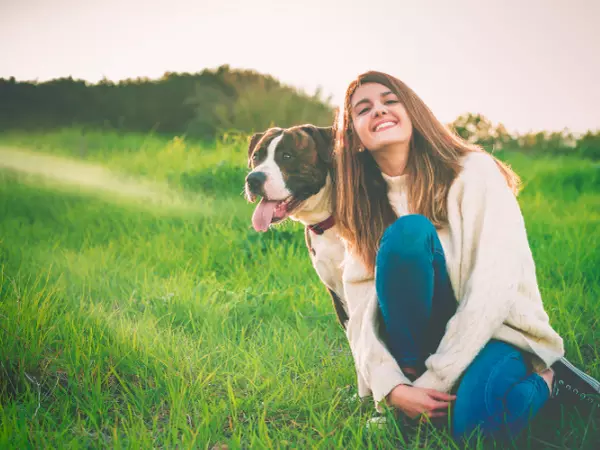 girl next to dog sitting on grass