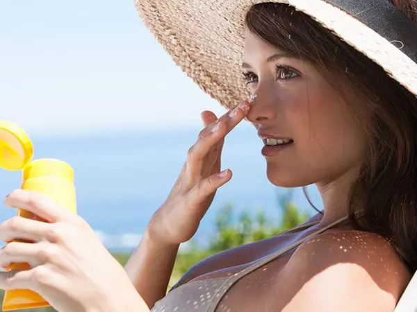 woman sitting outside in a chair with a hat on putting sunscreen on her nose