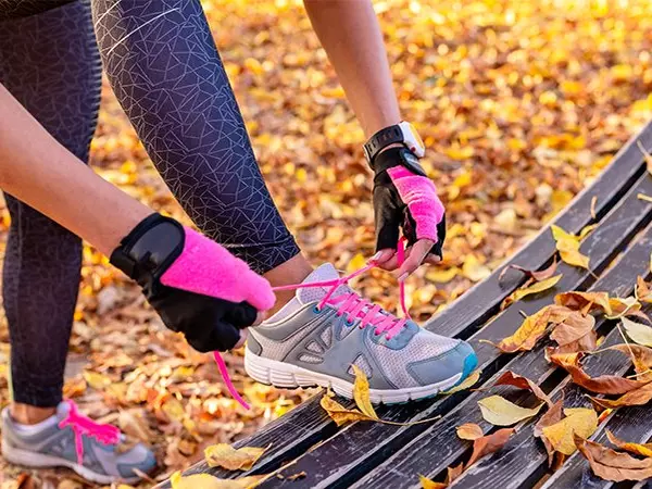 woman tying workout shoes in yellow fall leaves