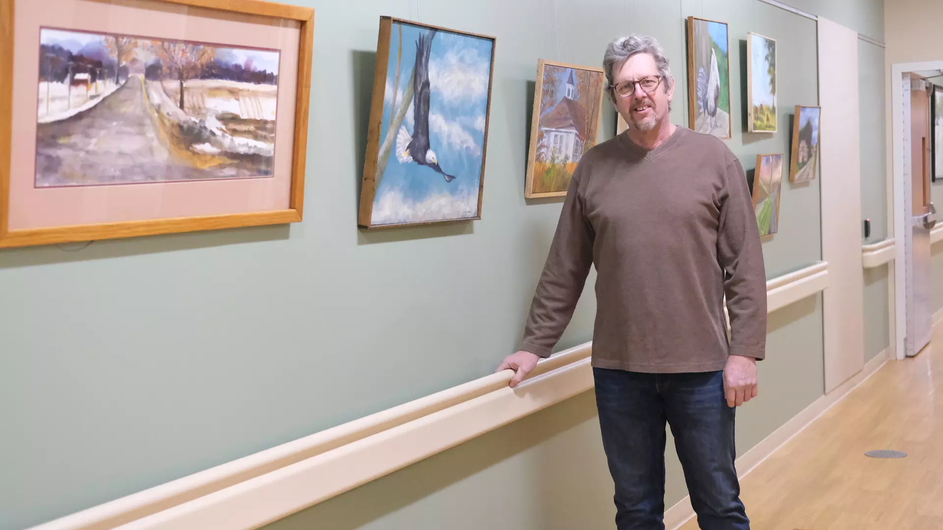 Local artist standing next to painting in hospital hallway.