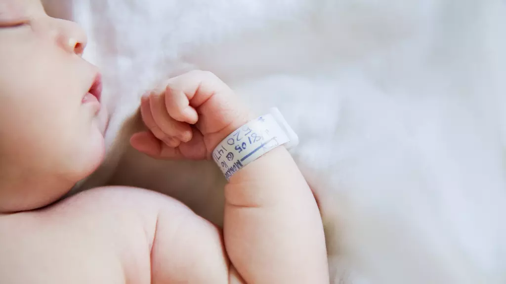Baby boy (9-12 months) sleeping with hospital bracelet on wrist, close-up.