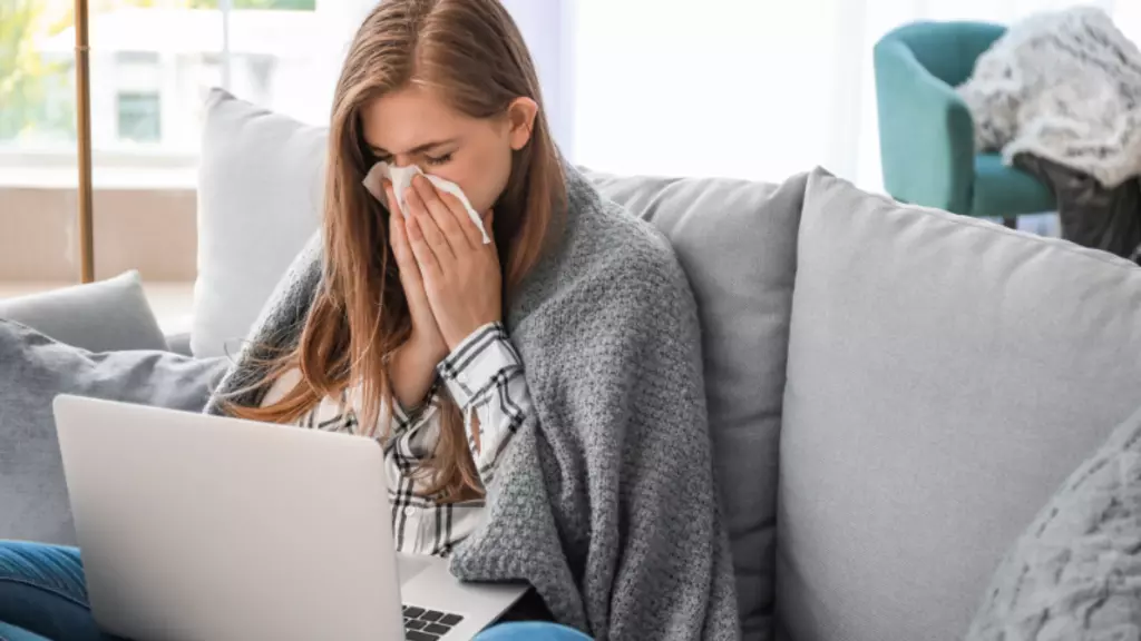 woman on a couch sneezing looking at a computer