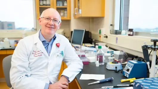 Cancer research scientist seated and smiling in clinical lab.