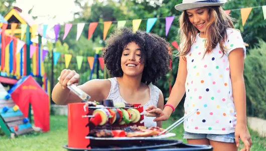 Woman and young girl standing in front of grill with meat and vegetables cooking