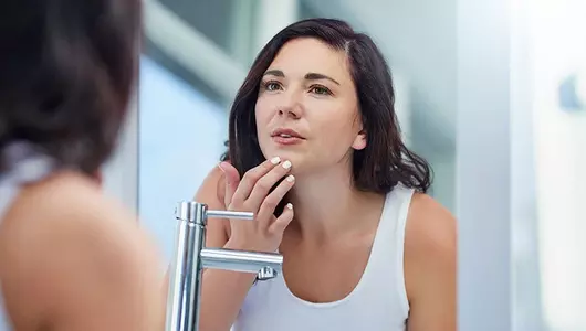 woman looking in the mirror at acne scars