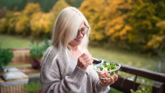 woman standing on balcony eating a salad