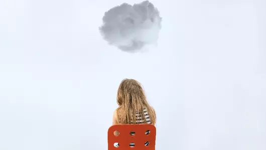 Adolescent girl sitting on a chair with a cloud hovering over her.