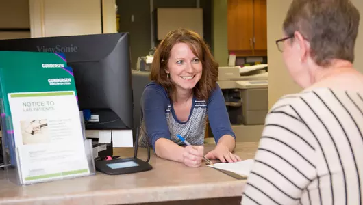 Healthcare receptionist greeting patient at front desk.