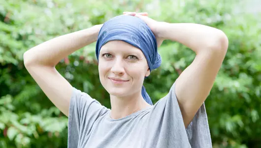 Young woman with cancer smiling with head wrap.