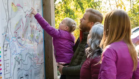 Family of four looking at hiking trails map in autumn.