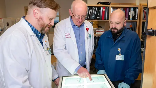 Three cancer research scientists looking at study data in lab.