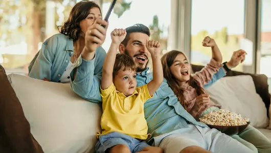 A cheerful family sitting on the couch watching a game on TV.