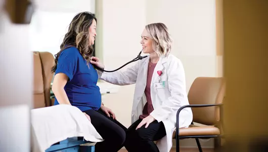 Young female doctor listening to pregnant woman's heartbeat.